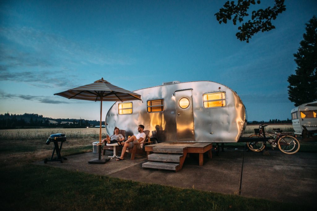 Young couple sitting outside their aluminum camping trailer at dusk